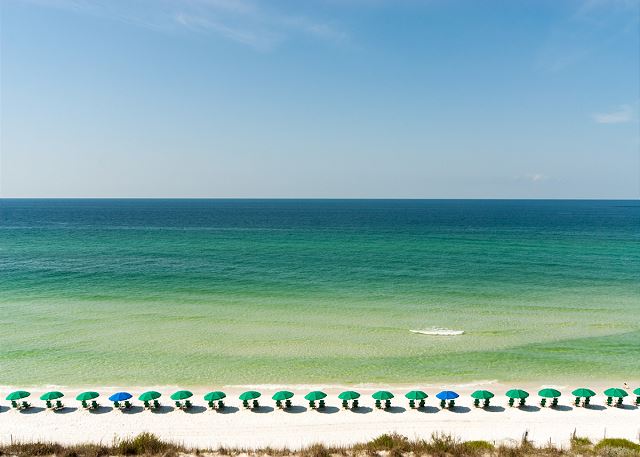 view of from one of our 30A rentals with a boat in the water and umbrellas lining the beach