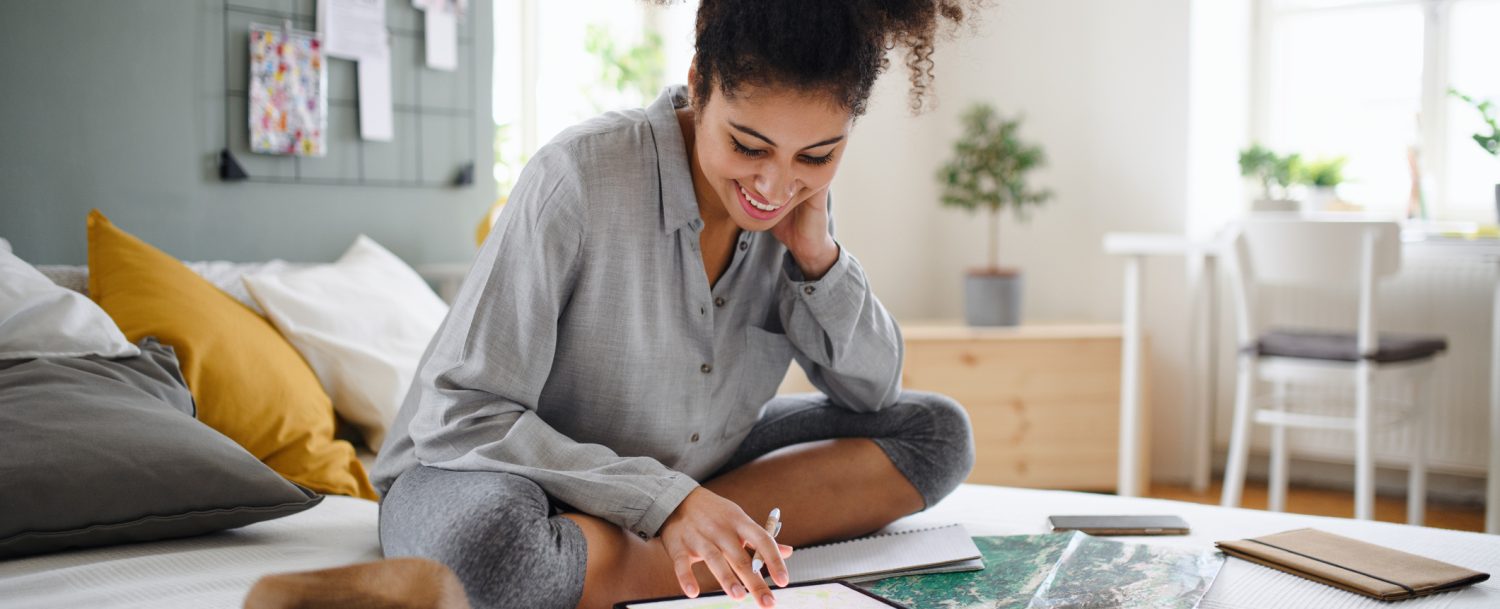 Young woman with tablet and map indoors at home, planning traveling trip. Solo female travel.