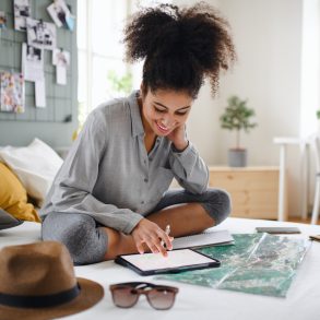 Young woman with tablet and map indoors at home, planning traveling trip. Solo female travel.