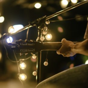Rear view of the man sitting play acoustic guitar on the outdoor concert with a microphone stand in the front, musical concept. Live music.