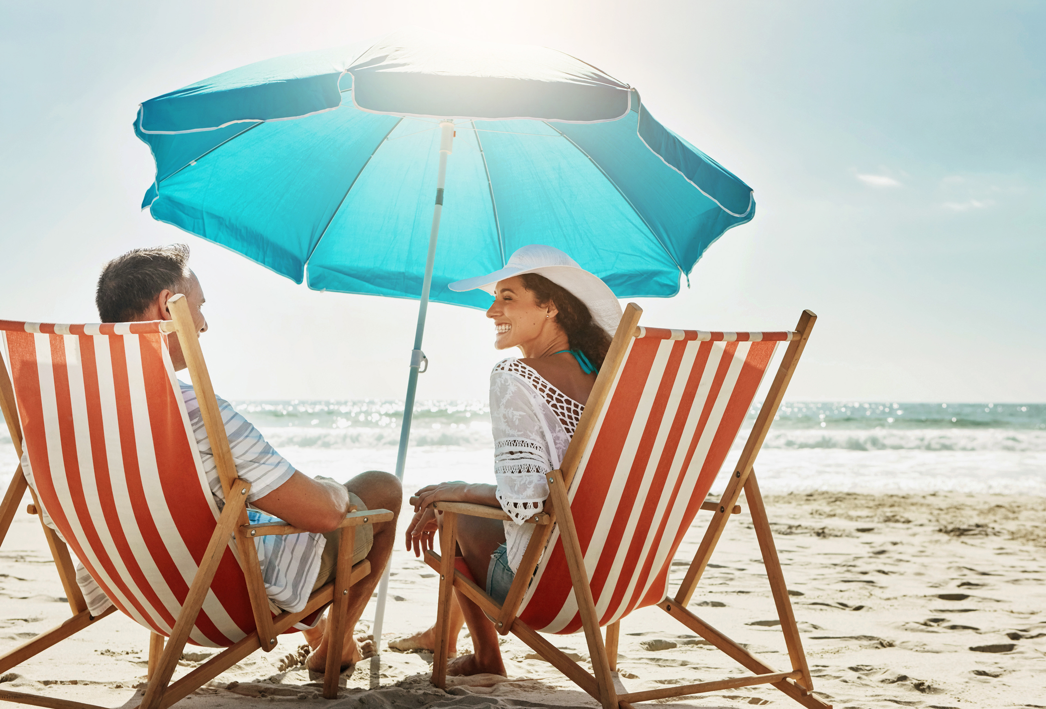 Beach, couple and relax chair for vacation adventure, bonding and love together in summer sunshine. Smile, woman and man with care, support and tropical holiday travel for ocean journey