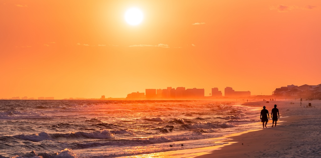Couple walking on shore with dramatic orange red yellow sunset in Santa Rosa Beach, Florida