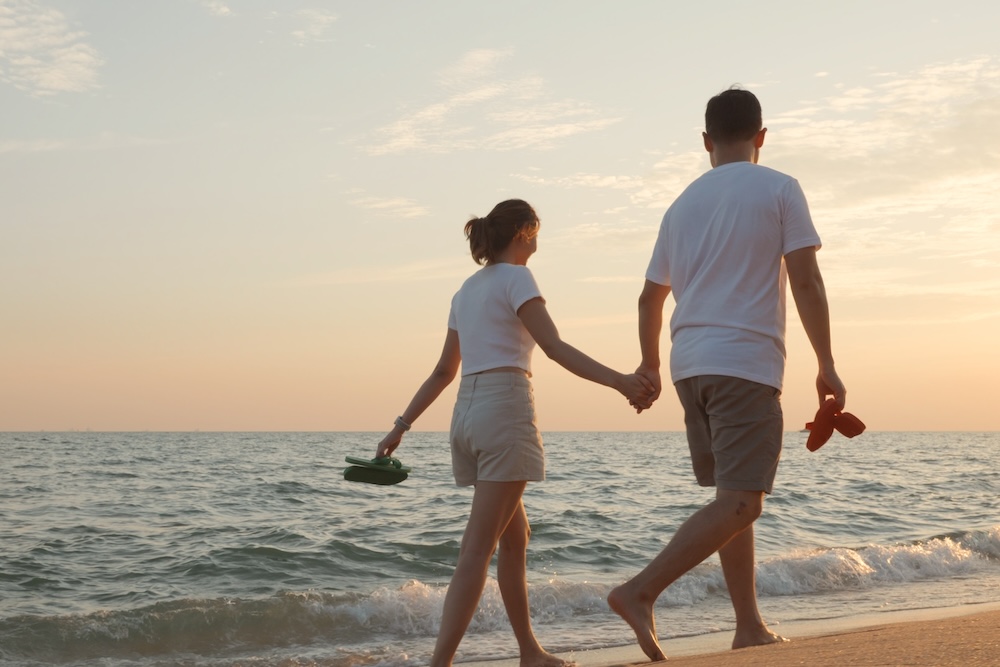 Vacation loving couple walking on beach together at sunset